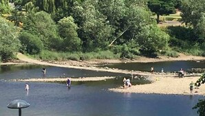 A riverside area with people engaging in water activities, surrounded by trees and a golf course in the background.