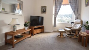 A living room with a television, wooden furniture, a potted plant, and a view through the window.