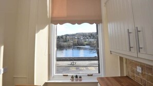 A kitchen with a view of a lake and a bench by the water.
