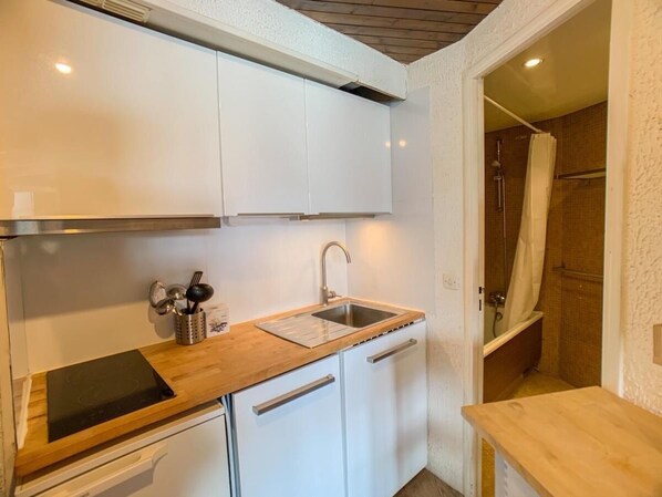 Eine kleine Küche mit weißen Schränken, einer Edelstahl-Spüle und einer Holz Arbeitsplatte.