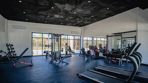 A gym with various exercise equipment, large windows, and a concrete ceiling.