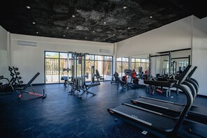 A gym with various exercise equipment, large windows, and a concrete ceiling.