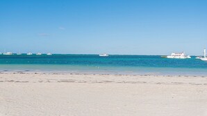 A beach with clear blue water and several boats.