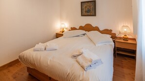 Una cama bien hecha con ropa blanca y toallas, dos lámparas de noche y un cuadro en la pared.