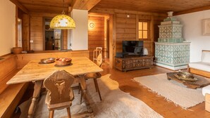 Interior de una cabaña de madera con una mesa de comedor, sillas, un televisor, un mueble decorativo y un sofá.