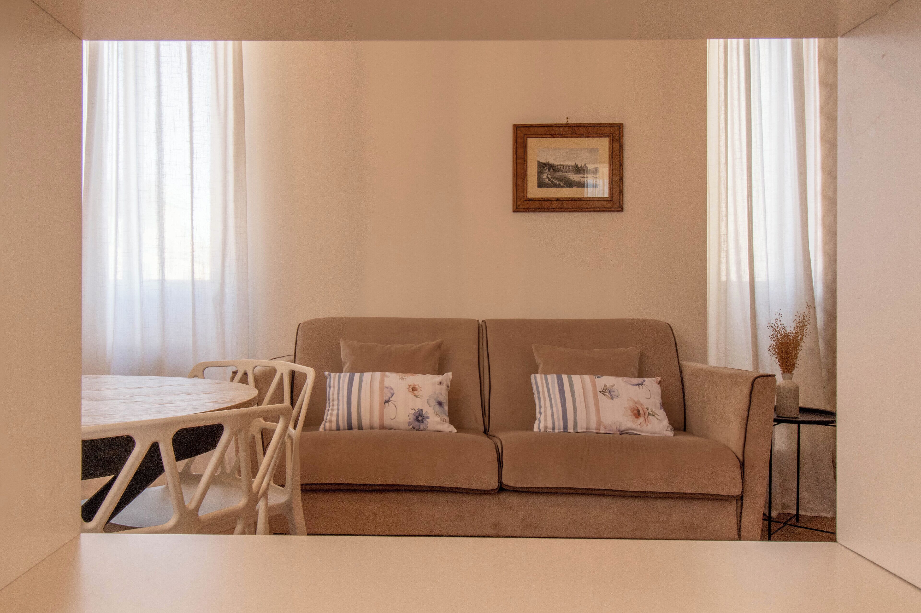 A living room with a beige sofa, two pillows, a round table, and chairs.