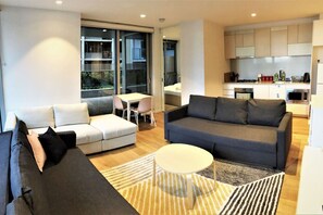 A modern living room with a grey sofa, a white armchair, and a small round table. There is a kitchen area with cabinets and a microwave. - 2x 2BR Apartment on Rose Lane (Melbourne)