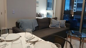 Ein modernes Wohnzimmer mit einer Couch, einem Esstisch gedeckt mit Tellern und Gläsern sowie einem Glastisch.