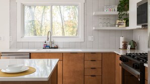 Una cocina moderna con un amplio ventanal, azulejos blancos, armarios de madera y una estufa a gas.
