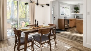 Un comedor con una mesa dispuesta para cuatro, una cocina al fondo y un patio exterior accesible por un ventanal corredero.