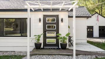 Stylish home with a clean design, featuring a front door with a glass panel, surrounded by a well-manicured lawn and a pergola.