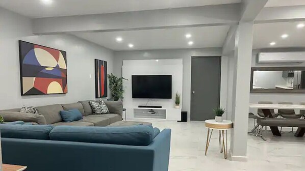 A modern living room with a large sofa, a flat-screen TV, and abstract art on the wall.