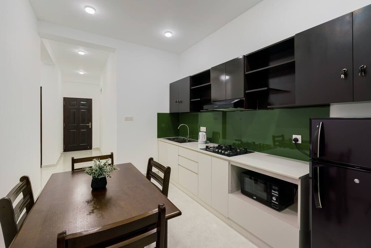 A modern kitchen with dark cabinets, a green backsplash, and a dining area with a wooden table and chairs.
