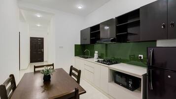 A modern kitchen with dark cabinets, a green backsplash, and a dining area with a wooden table and chairs.