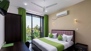 Hotelkamer met een groot bed, een bureau, een stoel, een plafondventilator, een airconditioning en uitzicht op palmbomen door het raam.