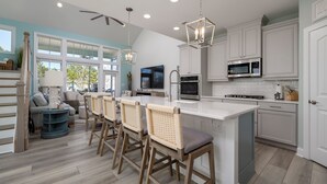 Una cucina moderna con mobili bianchi, un'isola centrale con sgabelli da bar, un forno a microonde integrato e una ventola a soffitto.