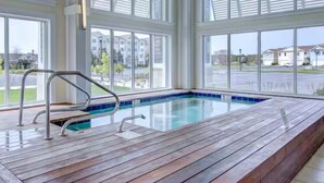 Una piscina con bordo in legno e ringhiere in metallo, ampie finestre e vista su edifici residenziali.