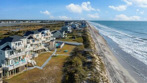 A coastal residential area with beachfront properties, including houses with balconies and a swimming pool, and a sandy beach adjacent to the ocean. - At Last - Oceanfront - 5 Bed, 4 Bath -  Pool, Hot Tub, Elevator & Backyard (North Topsail Beach)