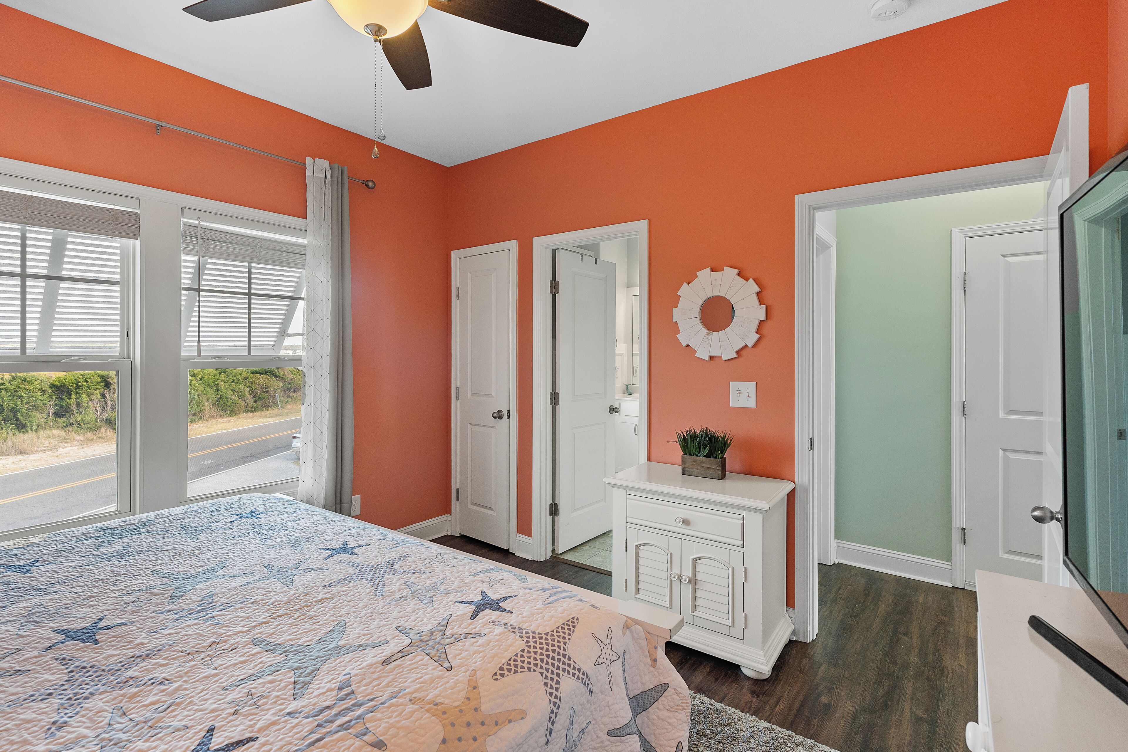 A bedroom with a bed, a ceiling fan, a dresser, and a door leading to another room.
