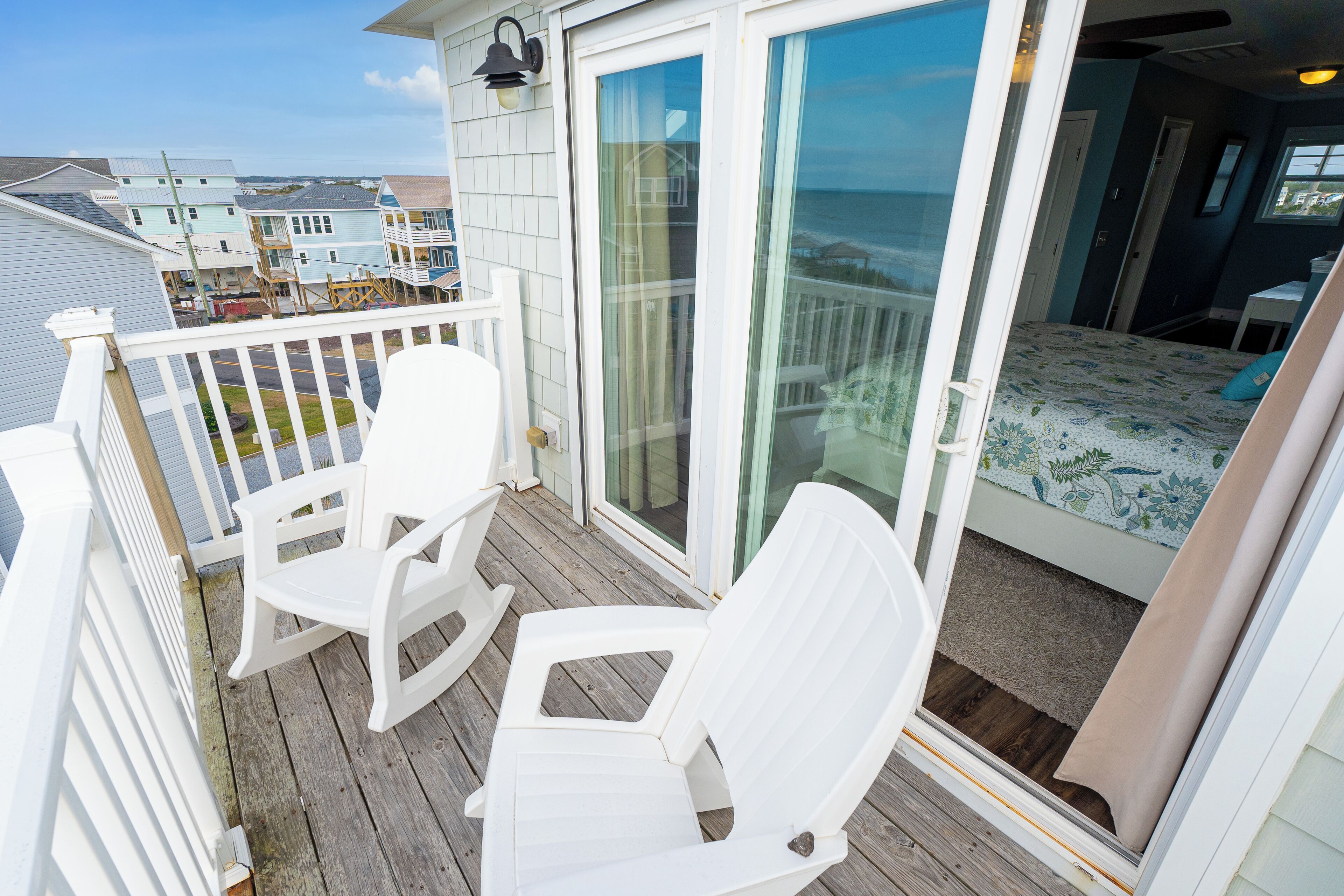 A balcony with white chairs, a bed with a floral bedspread, and a view of the ocean.