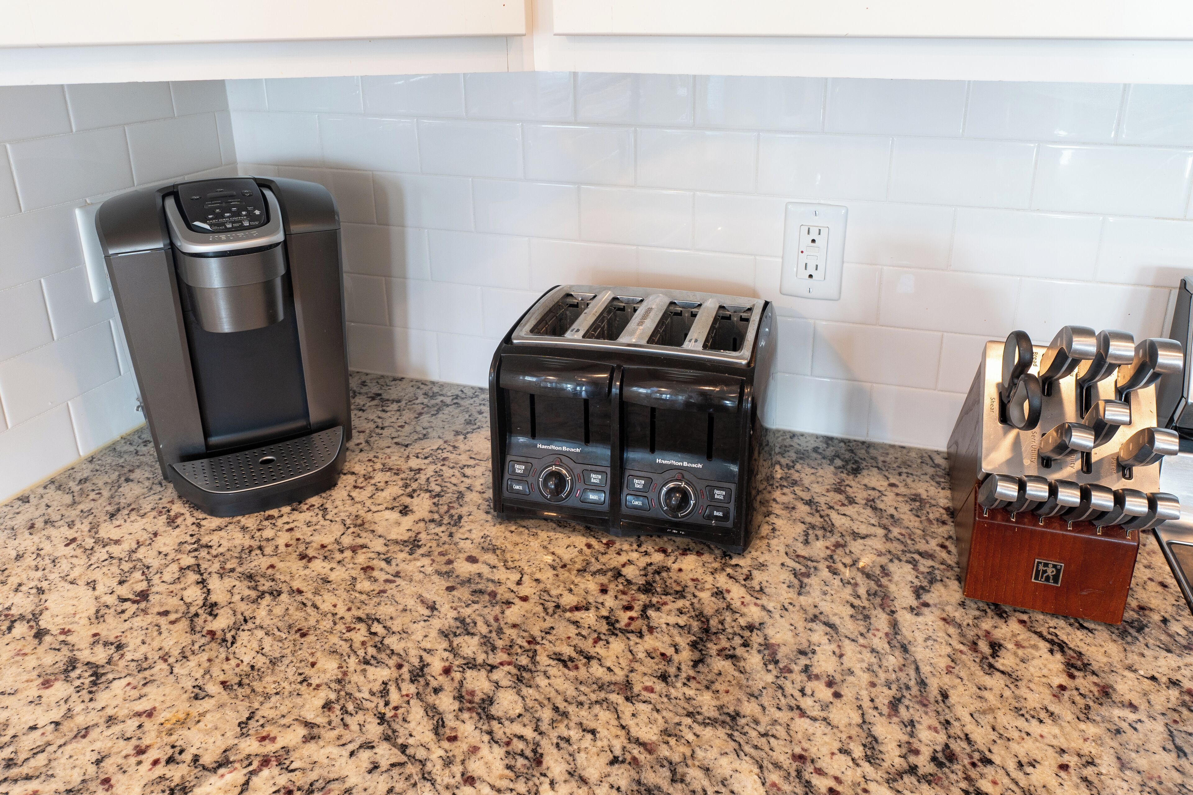 A kitchen with a coffee maker, toaster, and knife block on a granite countertop.