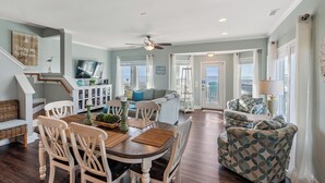 A spacious living area with a dining table, chairs, a sofa, and a patterned armchair. - At Last - Oceanfront - 5 Bed, 4 Bath -  Pool, Hot Tub, Elevator & Backyard (North Topsail Beach)
