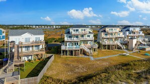 A coastal residential area with multi-story houses featuring balconies, a swimming pool, and a beach view. - At Last - Oceanfront - 5 Bed, 4 Bath -  Pool, Hot Tub, Elevator & Backyard (North Topsail Beach)