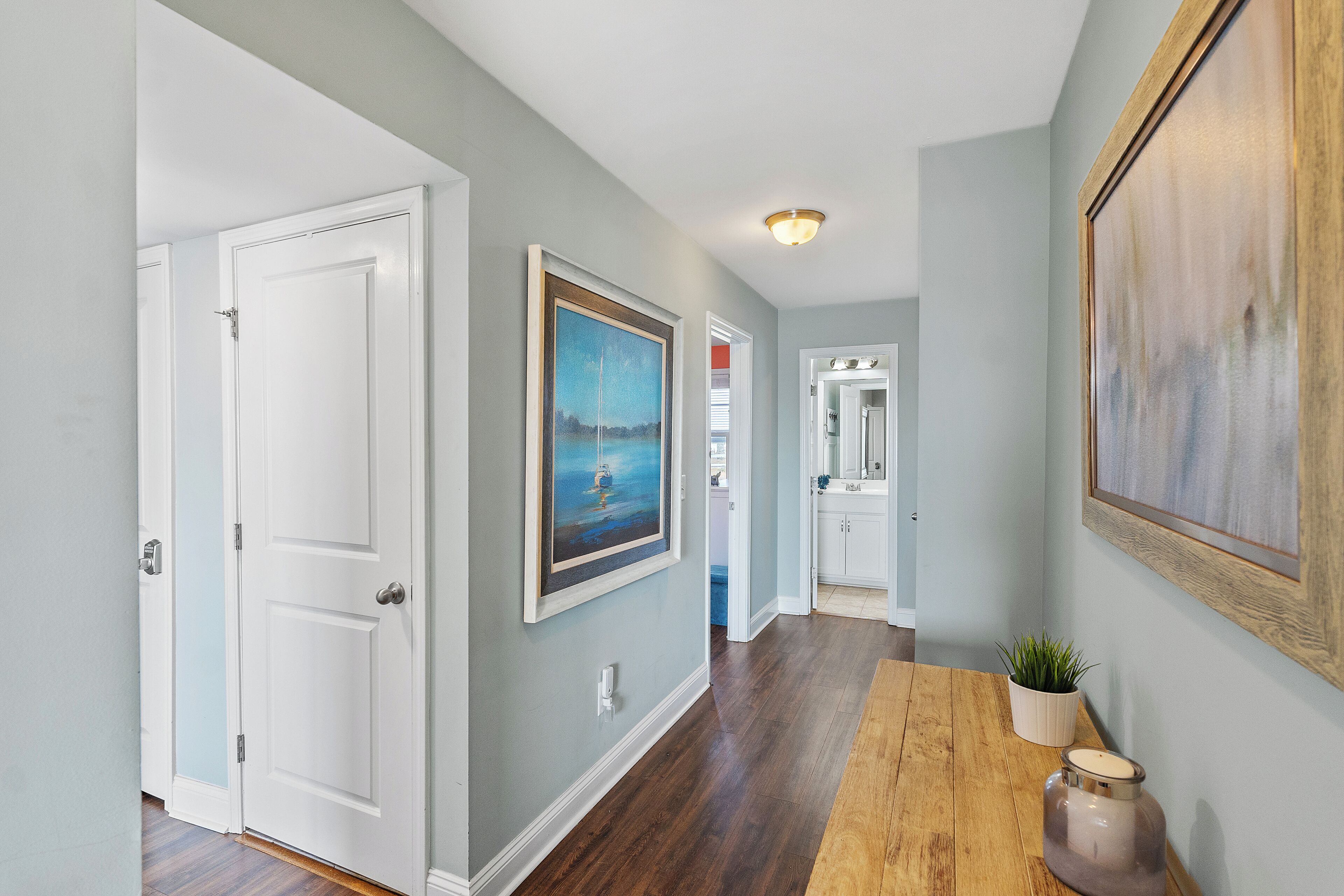 A hallway with wooden flooring, white doors, and framed artwork on the walls.