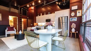 A modern kitchen with white cabinets, stainless steel appliances, and a dining area with a round table and wireframe chairs. - Studio loft with garage door with AC located in the heart of DTSA (Santa Ana)