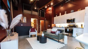A modern living room with a sofa, coffee table, and a dining area with a white table and chairs. - Studio loft with garage door with AC located in the heart of DTSA (Santa Ana)