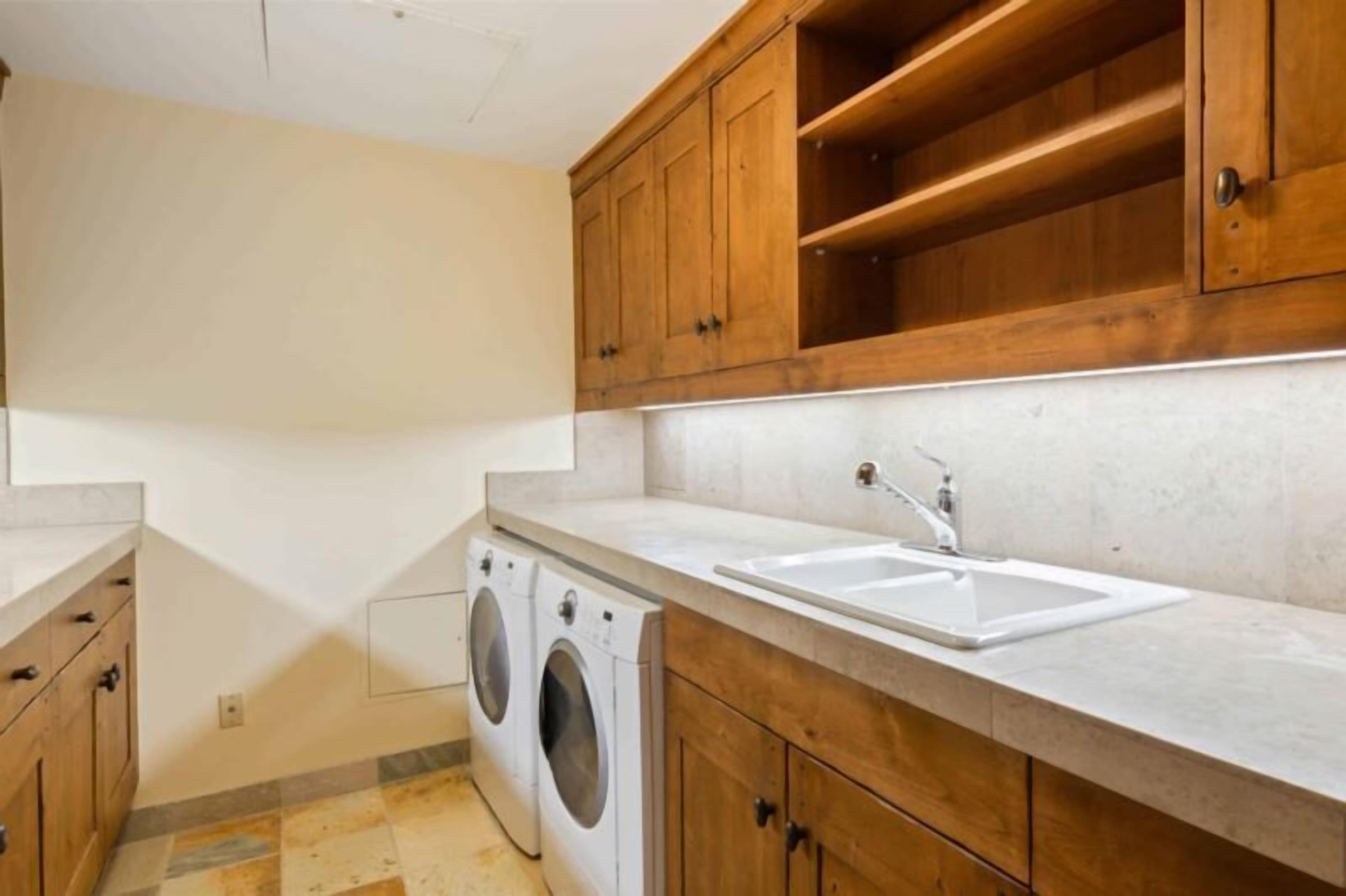 A laundry room with a washing machine, a sink, and wooden cabinets.
