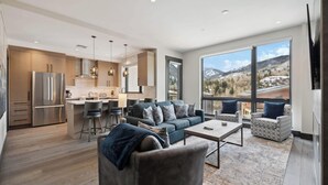 A spacious living area with a kitchen, large windows offering mountain views, and modern furnishings.