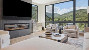 Een moderne woonkamer met een open haard, grote ramen en uitzicht op bergen.