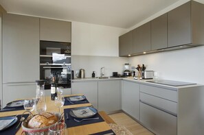 Une cuisine moderne avec des meubles de couleur grise, un four encastré et un coin repas avec une table mise pour deux personnes.