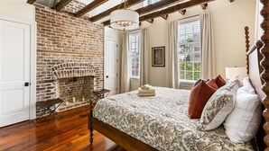 Une chambre avec une cheminée en briques, un lit en bois recouvert d’une couvre-lit à motifs et un lustre.