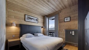 Un dormitorio con techo de madera, una cama con ropa de cama blanca, una mesita de noche con lámpara y vistas al exterior a través de una puerta.