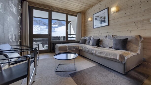 Un salón moderno con un sofá, una mesa de centro y vistas a montañas a través de grandes ventanales.
