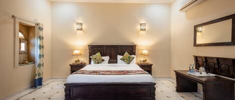 Habitación de hotel con una cama grande, dos lámparas de noche, una mesita de noche, un banco de madera y un espejo en la pared.