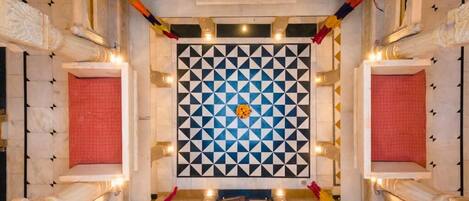 A room with a geometric patterned wall, a central chandelier, and a red curtain.