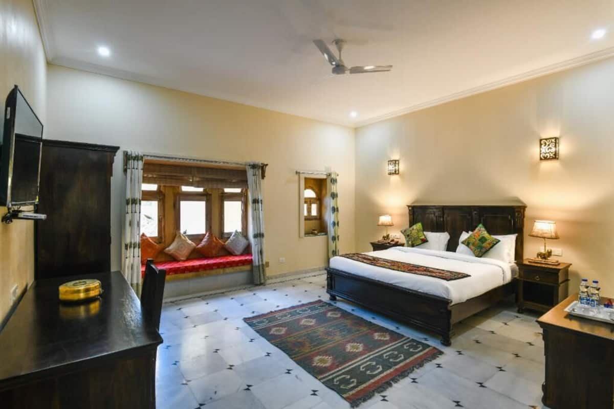 A hotel room with a large bed, a desk, a chair, a TV, and a window with curtains.
