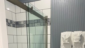A bathroom with a glass shower enclosure, a toilet, and a trash bin.