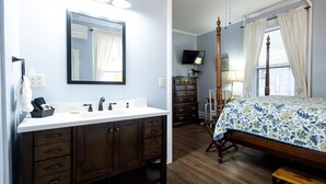 A bedroom with a wooden bed, a nightstand, a dresser, a television, and a large window with curtains.