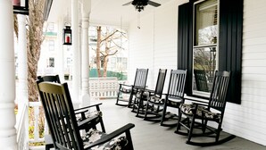 A porch with six rocking chairs and a white railing.