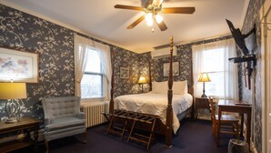 A bedroom with a four-poster bed, a chair, a desk, and a radiator.