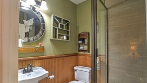Un baño con tocador de madera, lavamanos, inodoro y espejo con luces.