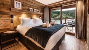 Une chambre à coucher aux murs lambrissés, avec un grand lit, une table de chevet et une vue sur un lac, visible à travers une grande fenêtre.