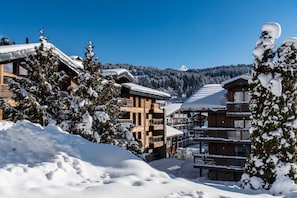 A snow-covered lodge with multiple wooden buildings, a ski slope in the background, and a clear blue sky. - Wifi, resort center, 4th floor, balcony, fireplace or stove, parking, tv, 181m², Les Gets (Les Gets)