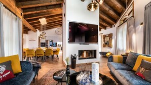 Un salon moderne avec une cheminée, un coin repas avec des chaises jaunes et un téléviseur fixé au mur.