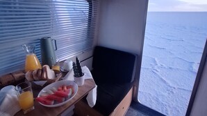 Pieni keittiönurkkaus, jossa on aamiaiselle katettu pöytä, ikkuna, josta avautuu näkymä merelle, ja penkkimäinen istuin.