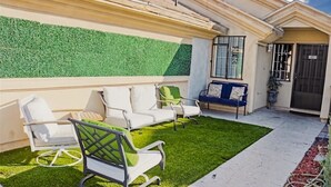 A patio with artificial grass, white outdoor furniture, and a green wall. - Charming 2-bedroom house in fantastic Las Vegas with AC, WiFi Casita los Hermano (Las Vegas)